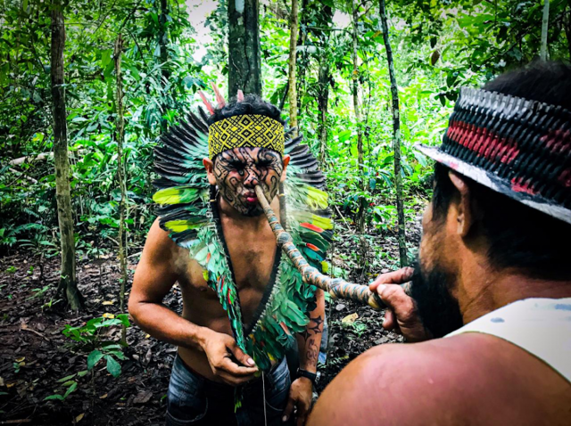 An Indigenous man dressed in traditional garb receives medicine through his nose via a long tube.